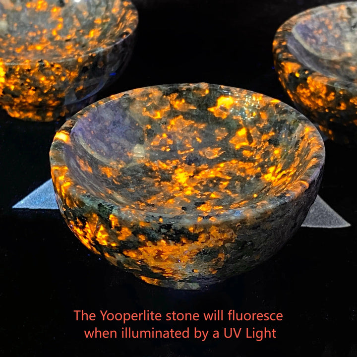 Yooperlite Crystal Bowl UV Reactive Glowing Stone Dish, vivid orange and gold patterns illuminate the polished grey vessel.
