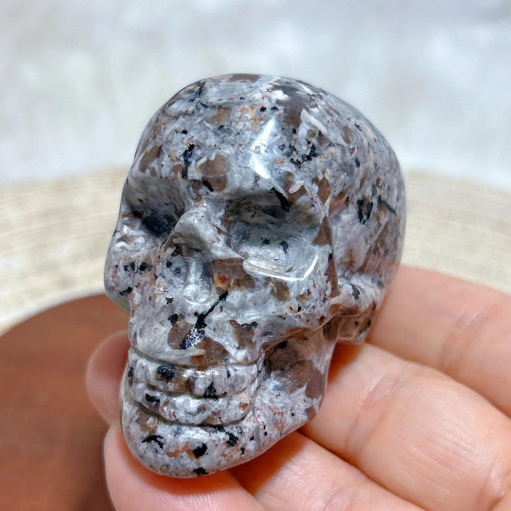 Yooperlite Crystal Carved Skull: detailed grey stone with black and brown flecks, held in a hand.