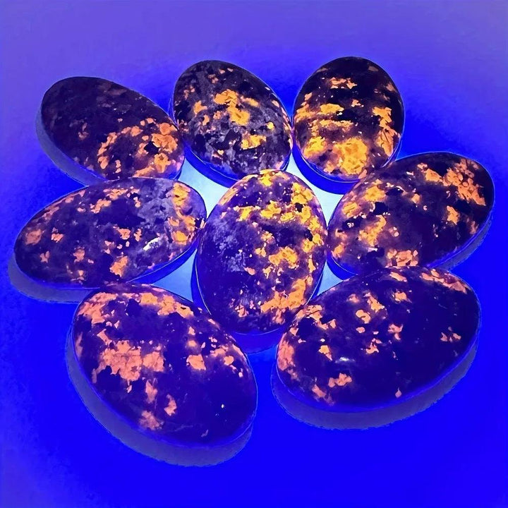 Yooperlite Crystal Palm Stone Flame UV Reactive Glow: Eight polished oval stones with vivid orange and gold patterns under blacklight.