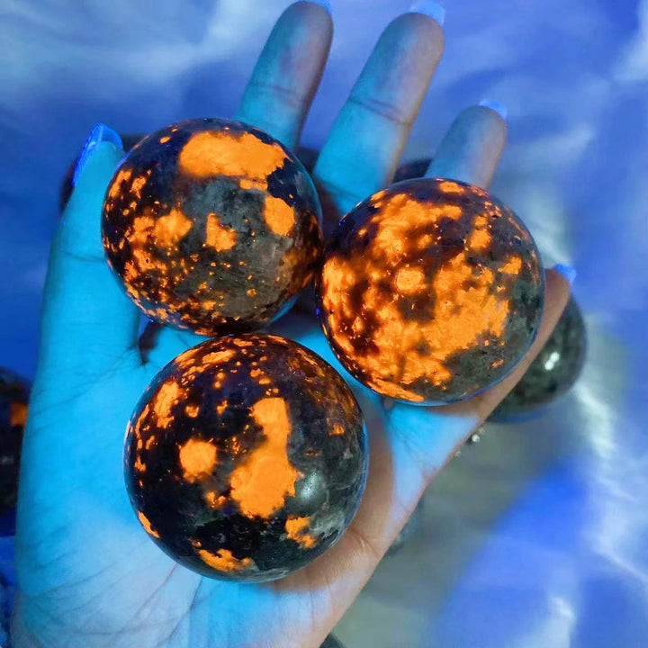 Hand holding three Yooperlite Crystal Sphere Flame UV Reactive Glowing Balls, blazing orange under blacklight.