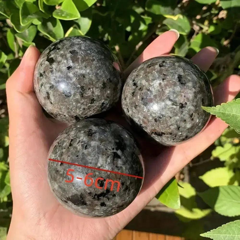 Three marbled gray Yooperlite UV Glowing Crystal Spheres, 5-6cm, held in a hand against green foliage.
