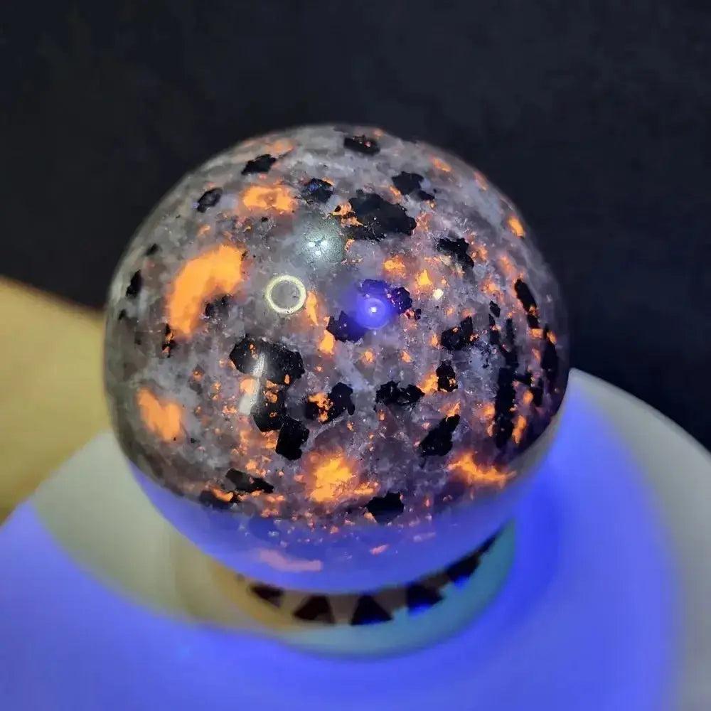 Yooperlite UV Glowing Crystal Sphere: Marbled gray sphere with fiery orange fluorescence under UV light, illuminating hidden emotions.