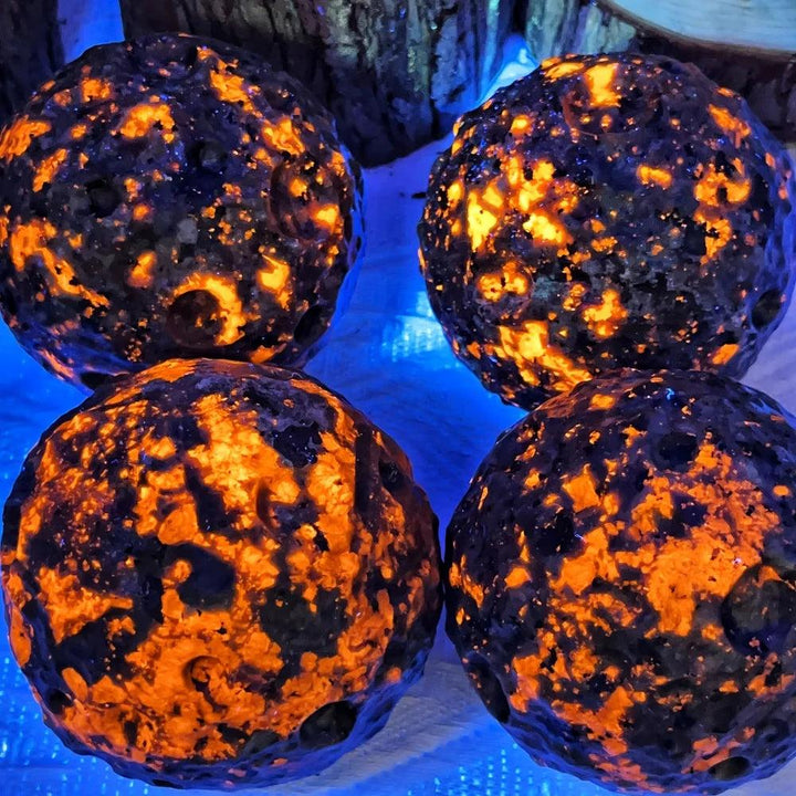 Four Yooperlite Crystal Spheres glowing vivid orange under UV light, perfect for grounding and manifestation.