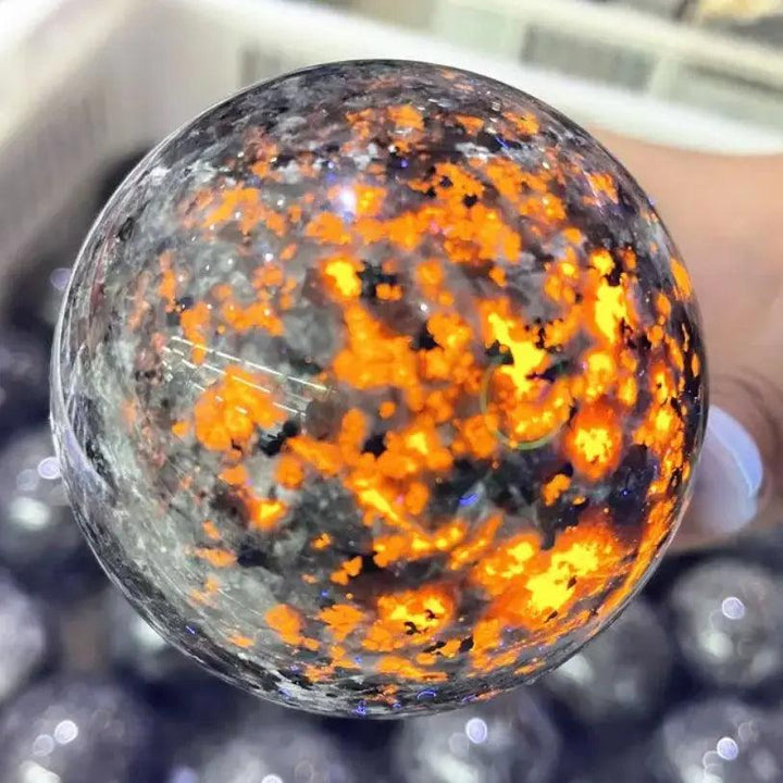 Polished Yooperlite crystal sphere glowing with vivid orange fluorescent sodalite under UV light for grounding energy.