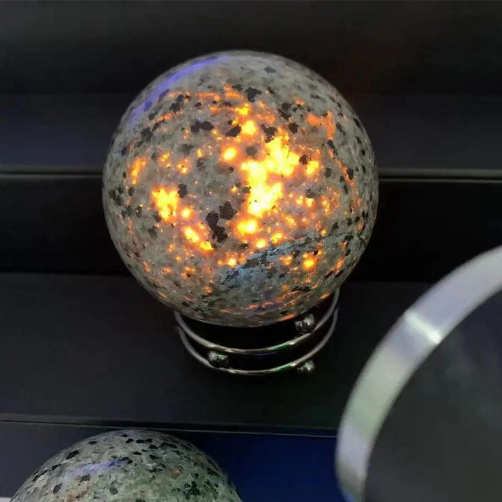 Polished Yooperlite crystal sphere glowing with vivid orange fluorescent sodalite under UV light for grounding energy.