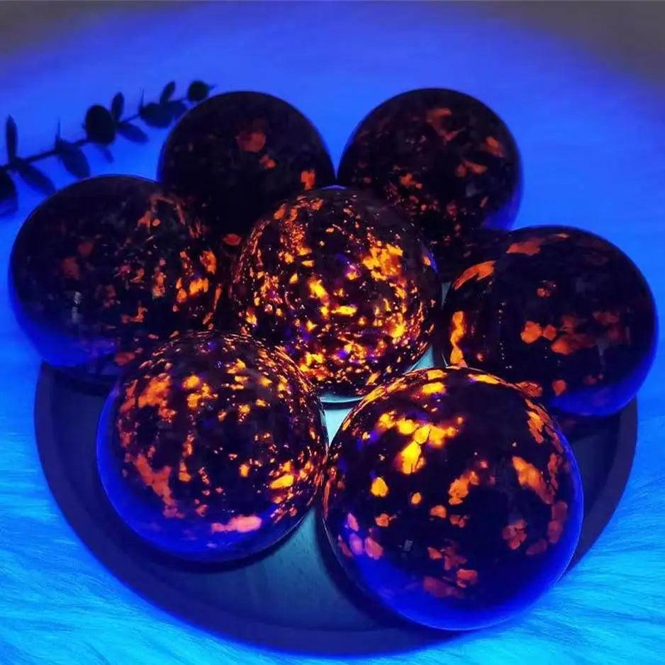 Polished Yooperlite crystal spheres glowing with vivid orange fluorescent sodalite under UV light for grounding energy.
