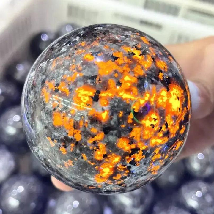 Polished Yooperlite crystal sphere glowing with vivid orange fluorescent sodalite under UV light for grounding energy.