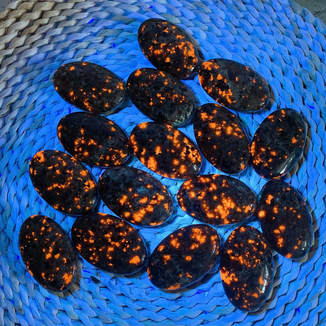 Polished Yooperlite palm stones glowing with vivid orange fluorescent sodalite under UV light for grounding energy.