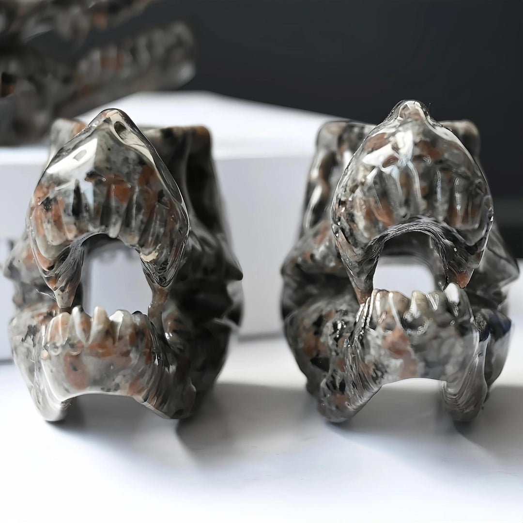 Two small, shiny Yooperlite T-Rex skull carvings in warm brown and gray tones, showing intricate details.